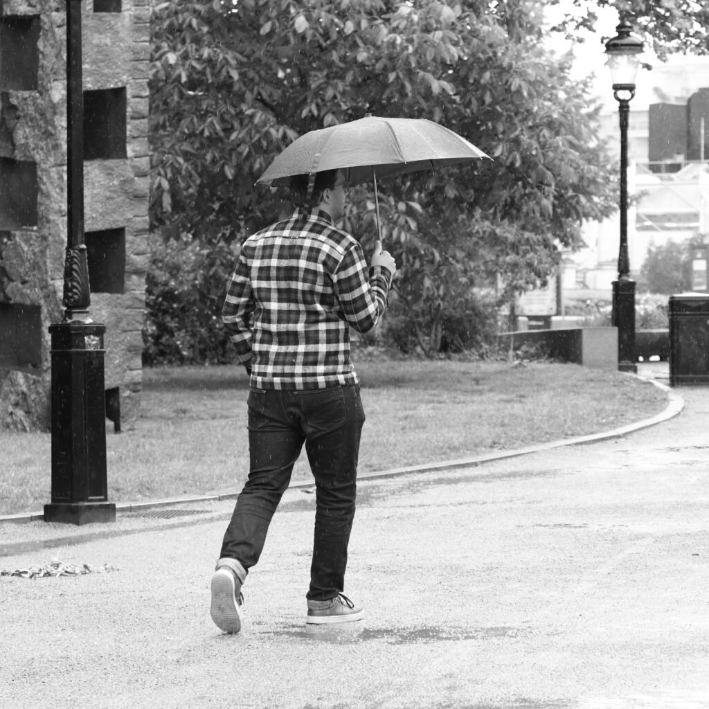 A man walks through a park in Lund, Sweden with an umbrella during a rainy day.