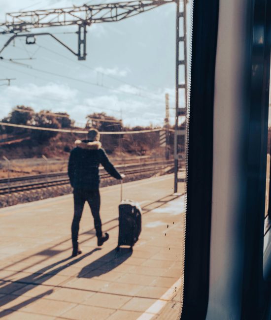 A man walks on a train platform with luggage, viewed from a train window.