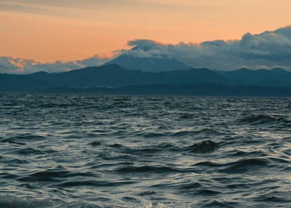 Calm ocean waves and mountains under vibrant sunset skies.